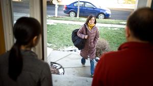 Student walking up the sidewalk to greet parents standing in the doorway