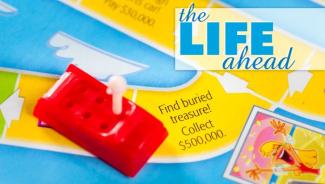 A plastic red car on the board from the board game "Life", and the words "The Life Ahead"