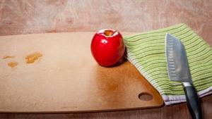 Red apple on cutting board next to kitchen knife on towel