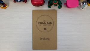 a small canvas notebook with "Just Tell Me What I Need to Know" on its cover