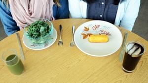 Two people sitting at a table. One has a salad, and the other has a twinkie on a plate.