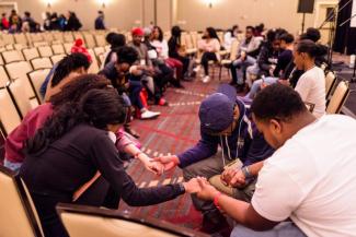 Group of Black students praying in circle holding hands