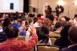 People in an auditorium raising their hands towards the stage