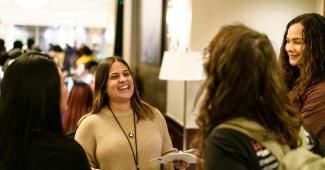 Group of four women talking and laughing in hotel hallway outside of conference session