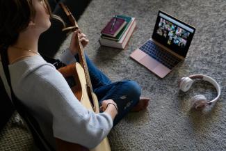 Student sitting on floor playing guitar leading virtual worship