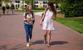 Campus minister Liv Brazer on campus walking down sidewalk talking to female student 