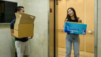 Two students moving into dorm, holding cardboard boxes