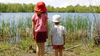 two children, one tall and one short, standing side-by-side and looking out over a lake