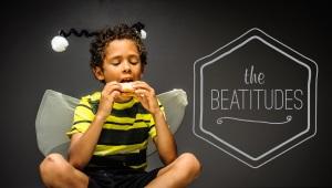 Young boy in bee costume sitting, eating sandwich with the words "The Beatitudes" in the background.