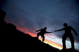 Silhouettes of two people climbing mountain at twilight