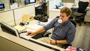 a man sitting in a cubicle blowing a bubble with gum