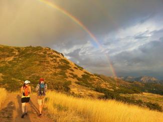 Two people hiking up a trail with cloudy sky and rainbow