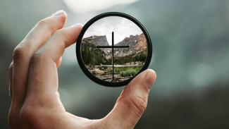 Hand holding camera lens focused on cross with blurry background