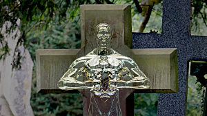 A gold statue standing perfectly in line with a wooden cross right behind it.