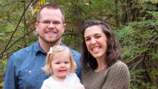 Photo of Ryan with wife and infant daughter standing in forest