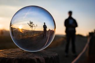  A bubble reflecting the image of a person standing in a desert landscape with a sunset behind them