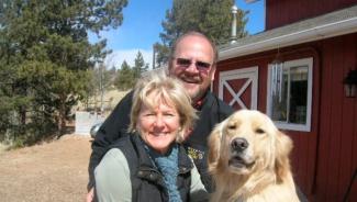 a man, woman, and dog smiling in front of a red barn