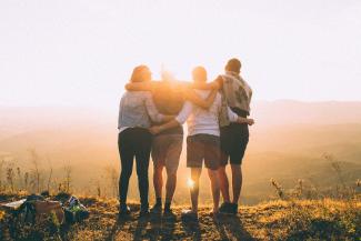 Four friends standing arm in arm and facing a sunset