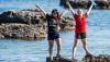 Two young women standing at the edge of the water with their arms thrown up in the air