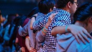 Group of people in auditorium standing with arms around each other