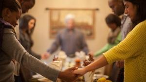 people of different ethnicities holding hands and praying across a dinner table