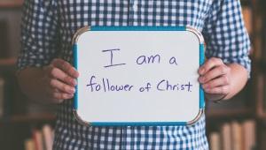 Man holding whiteboard that says "I am a Follower of Jesus"