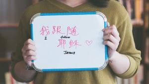 Woman holding whiteboard that says "I am a Follower of Jesus" in English and Chinese characters