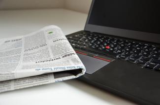 A newspaper resting on the corner of an open laptop computer