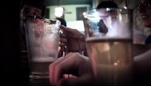 a glass cup half-full with beer and a half-empty beer pitcher on a bar