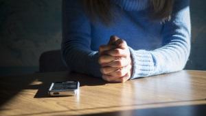 Person seated at table with hands folded next to a smartphone