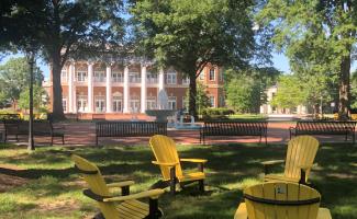 three yellow chairs on a campus quad with an academic building in the background