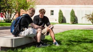 Two male students sitting on a bench on campus talking