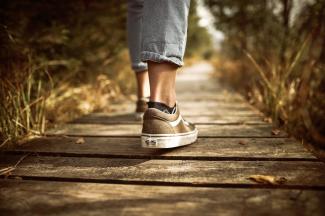 Feet wearing sneakers walking on a forest path.