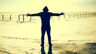 a silhouetted person standing by the water with arms open wide