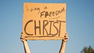 Hands of person holding cardboard sign with the words "Living is Freedom through Christ"