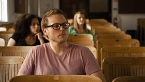 Several students sitting in chairs listening to lecture. Student in front is listening with serious interest.