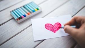 hand coloring a dark pink heart on a small white sheet of paper