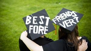 Two college graduates in cap and gown with "Best Friends Forever" written on their caps