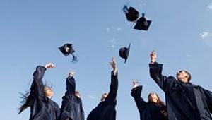 Group of graduates in gowns throwing caps up into air in celebration