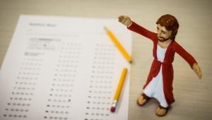 Jesus action figure standing next to standardized test and broken pencil