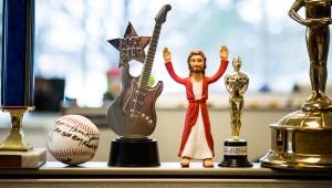 Jesus action figure standing between various golden trophies and autographed baseball