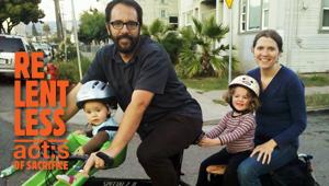 Mother and father posing with two young children outside of home with the label: Relentless Acts of Sacrifice