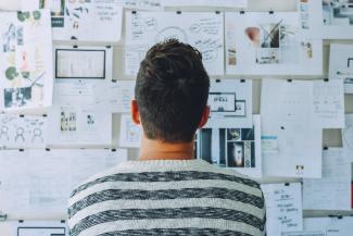 Man wearing black and white stripe shirt looking at a wall filled with design clippings