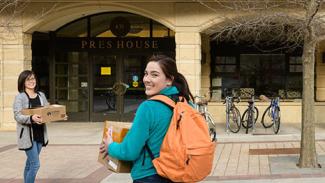 Student and mother walking with boxes toward campus building