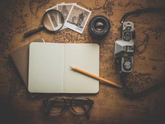  A pencil on white notebook near eyeglasses and a camera