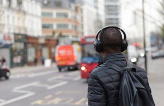 Closeup of young man wearing headphones standing on city street corner