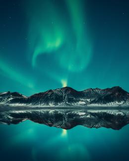 Green and blue Northern Lights shimmering above mountain and lake landscape