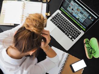 Woman looking stressed, holding her head surrounded by computer and notebooks