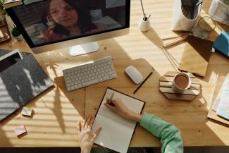 Person sitting at cluttered desk in front of computer taking notes