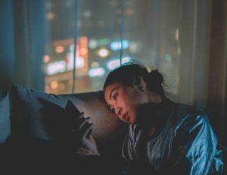 Woman sitting in dark room staring at phone. Window in the background of night cityscape.